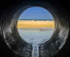 Bezpłatne zdjęcie spójrz z rury patrząc na plażę otoczoną morzem z ludźmi w niej oświetlonymi światłem słonecznym