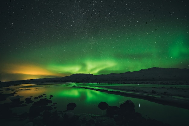 Spokój wody w pobliżu góry pod zorzą polarną w porze nocnej