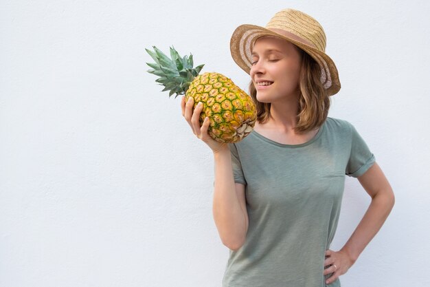 Spokojna inspirowana kobieta w letnim kapeluszu pachnącym ananasem