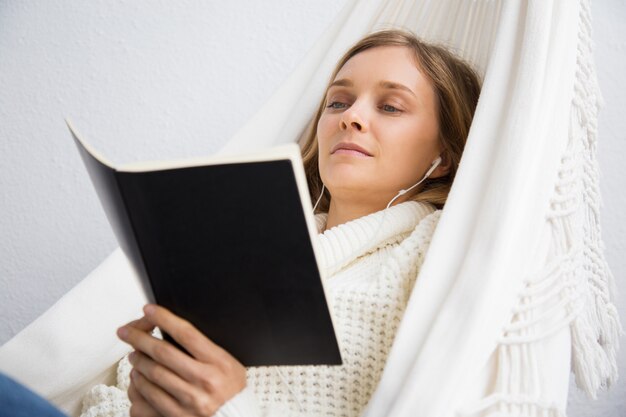 Spokojna młoda kobieta czytanie książki i słuchanie muzyki