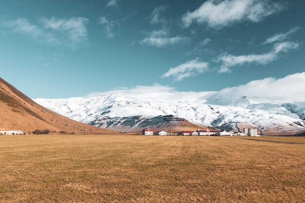 Spokojny widok na brązowe pole z domami z czerwonymi dachami i zaśnieżonymi górami w