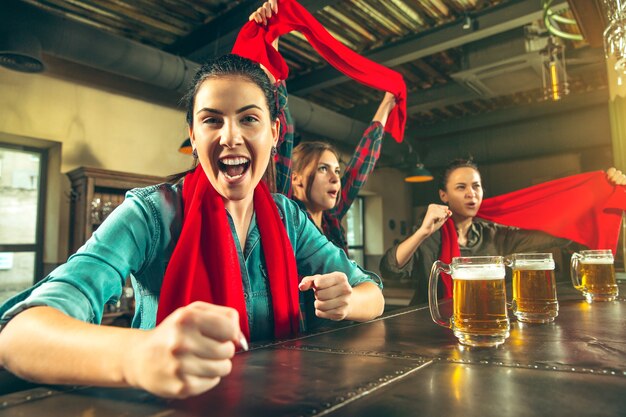 Sport, ludzie, wypoczynek, przyjaźń, rozrywka - szczęśliwe kibice lub dobre młode przyjaciółki pijące piwo, świętujące zwycięstwo w barze lub pubie. Koncepcja ludzkich pozytywnych emocji