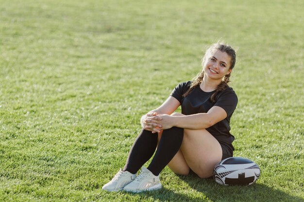 Sportive kobieta siedzi na trawie obok piłki