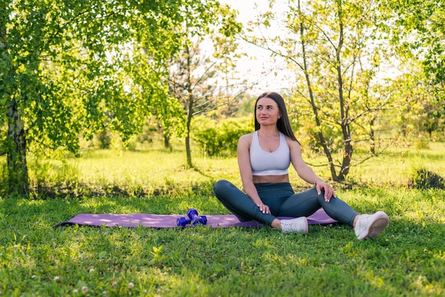 Sportowa młoda kobieta siedzi na macie sportowej i relaksując się po treningu na świeżym powietrzu