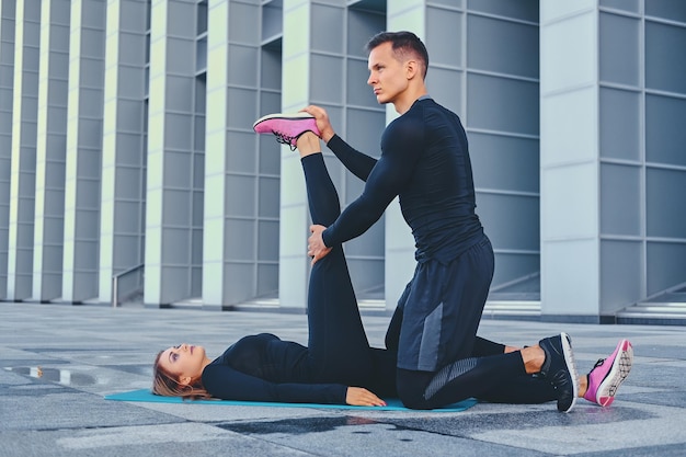 Sportowa para fitness ćwiczy na macie do aerobiku na tle nowoczesnego budynku.