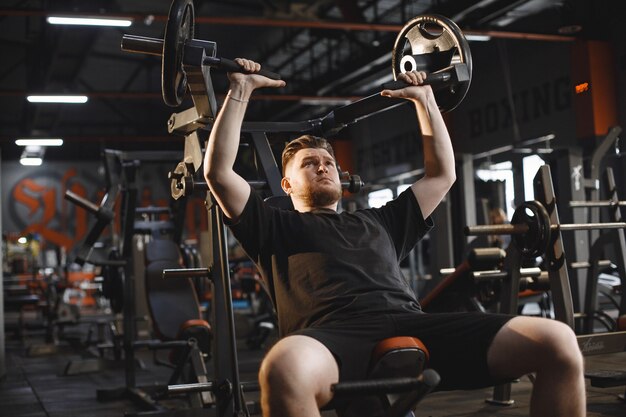 Sportowiec na siłowni. Mężczyzna wykonuje ćwiczenia. Facet w koszulce