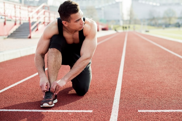 Sportowiec sprinter przygotowuje się do biegania wiązanie sznurówki do butów na bieżni stadionowych