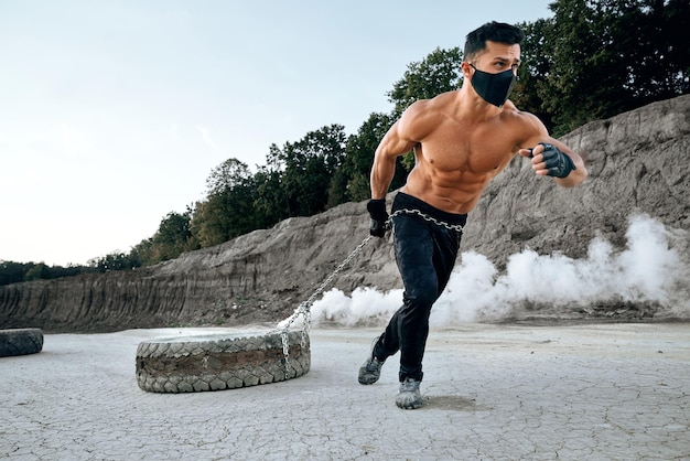 Bezpłatne zdjęcie sportowiec w czarnej masce używający ciężkiej opony do treningu