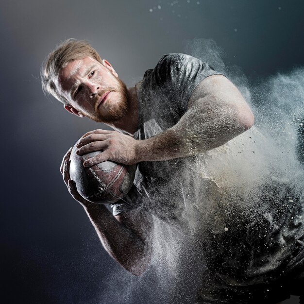 Sportowy męski gracz rugby trzymając piłkę z pyłem