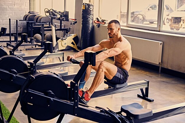 Sportowy półnagi mężczyzna robi treningi na plecach z maszyną do ćwiczeń mocy w klubie gimnastycznym.