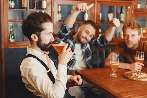 Spotkanie z najlepszymi przyjaciółmi. Trzech szczęśliwych młodych mężczyzn w casual rozmawia i pije piwo siedząc razem w barze.