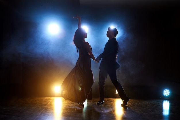 Sprawni tancerze występujący w ciemnym pokoju pod koncertowym światłem i dymem. Zmysłowa para wykonująca artystyczny i emocjonalny taniec współczesny