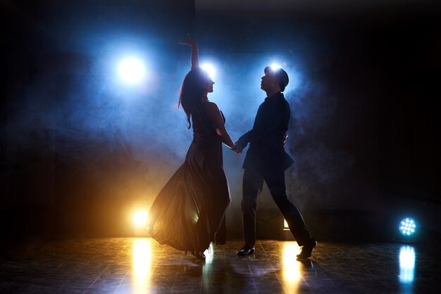 Sprawni tancerze występujący w ciemnym pokoju pod koncertowym światłem i dymem. Zmysłowa para wykonująca artystyczny i emocjonalny taniec współczesny