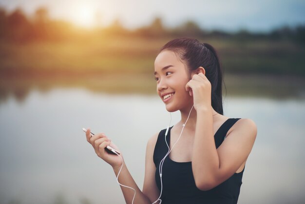 Sprawności fizycznej kobieta słucha muzykę podczas jej treningu i ćwiczenia w parku w słuchawkach