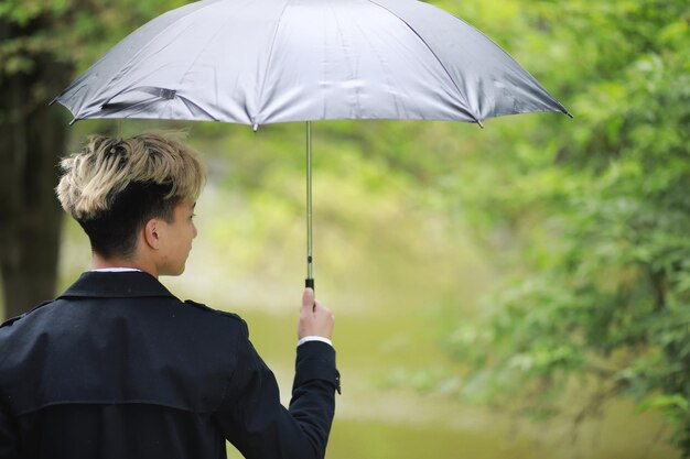 Spring park w deszczową pogodę i młody mężczyzna z parasolem