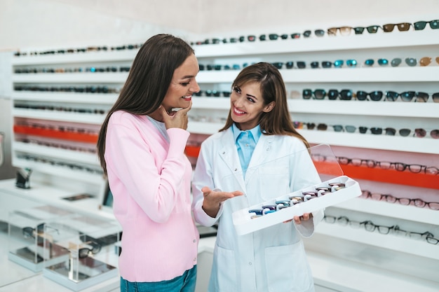 Sprzedawca kobiet w średnim wieku i klient wybierający nowe okulary w nowoczesnym sklepie optycznym. koncepcja zakupów.