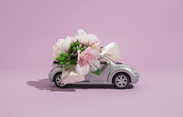 Srebrny kabriolet mały model samochodu z kwiatami na fioletowym tle. koncepcja dostawy kwiatów i prezentów na święta i uroczystości
