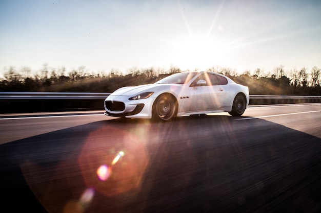 Srebrny samochód sportowy wysokiej prędkości jadący autostradą w słoneczną pogodę.