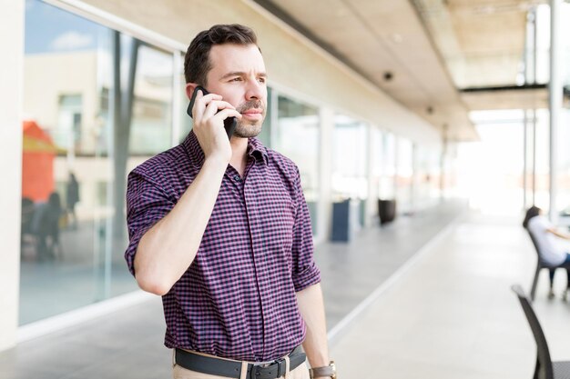 Średni dorosły mężczyzna odbiera telefon na smartfonie, stojąc w centrum handlowym