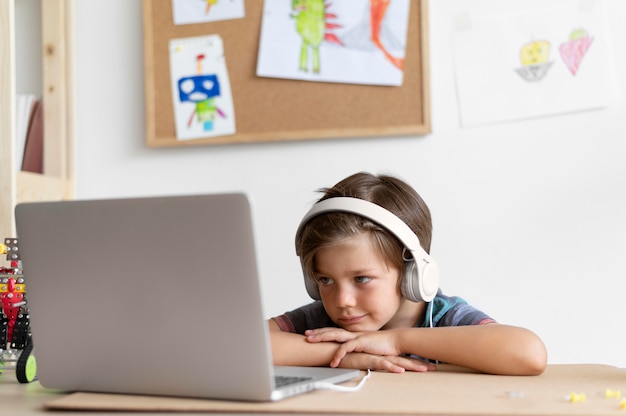 Średnie zdjęcie dzieciaka siedzącego przy biurku z laptopem