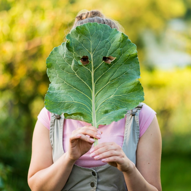 Bezpłatne zdjęcie Średnio strzał dziewczyna zakrywająca twarz liściem