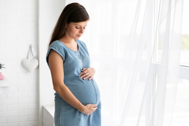 Średnio Strzał Kobiety W Ciąży Stojącej Obok Okna Premium Zdjęcia