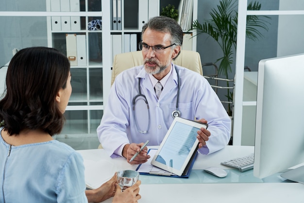 Średnio strzał lekarza w średnim wieku wyjaśniającego diagnozę za pomocą komputera typu tablet