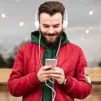 Bezpłatne zdjęcie Średnio strzał uśmiechnięty facet ze słuchawkami, patrząc na smartfona