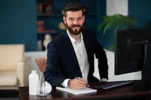 Bezpłatne zdjęcie Średnio strzał uśmiechnięty mężczyzna siedzący przy biurku