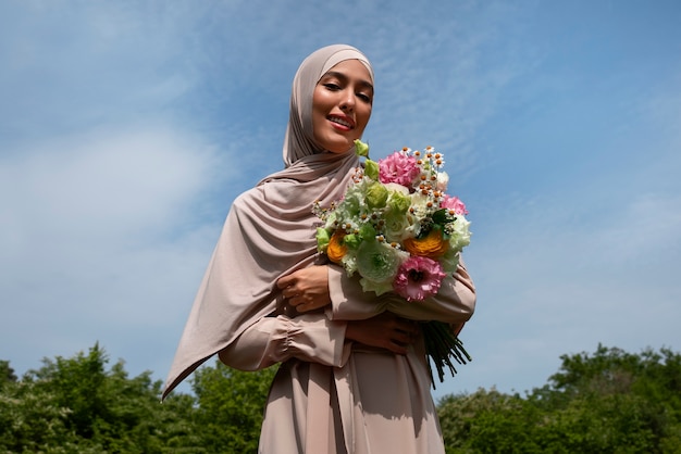Bezpłatne zdjęcie Średnio strzelająca muzułmańska kobieta pozuje z kwiatami