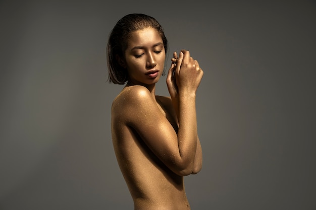 Bezpłatne zdjęcie Średnio wystrzelona kobieta pozująca ze złotym malowaniem ciała