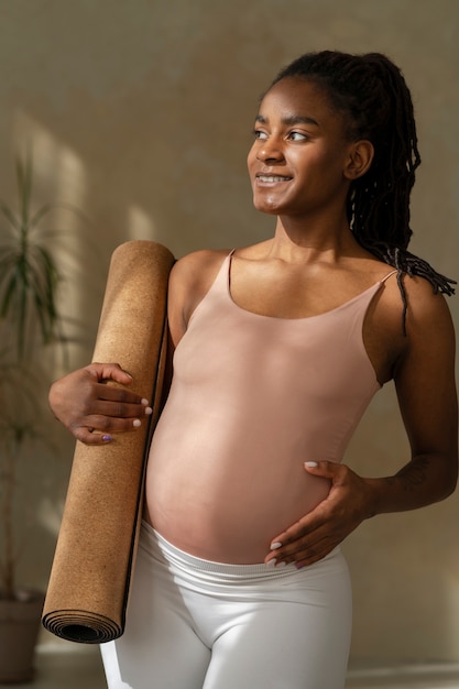 Bezpłatne zdjęcie Średnio zastrzelony kobieta w ciąży trzymająca matę do jogi
