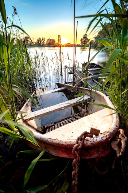 Bezpłatne zdjęcie stara żelazna łódź wiosłowa częściowo zatopiona na nabrzeżu stawu o zachodzie słońca