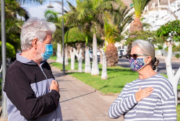 Starsi ludzie noszący maskę chirurgiczną spotykają się w publicznym parku i witają się z ręką na sercu