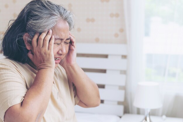 Starsi pacjenci w łóżku, Azjatyckie starszej kobiety pacjentów bólu głowy ręki na czole - medyczny i opieka zdrowotna pojęcie