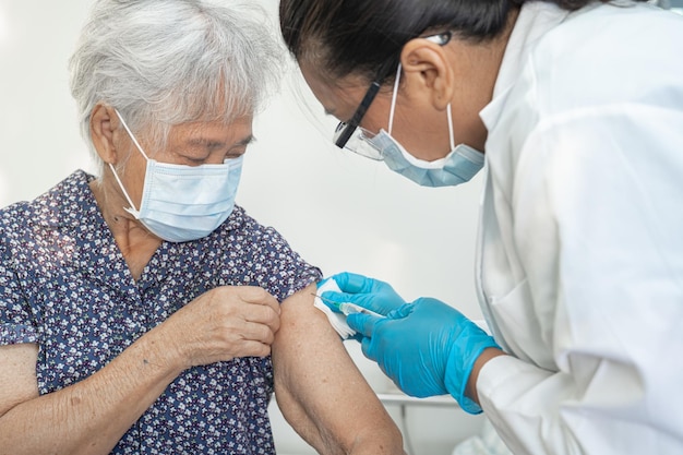Starsza azjatycka starsza kobieta nosząca maskę na twarz, która otrzymuje przez lekarza szczepionkę przeciwko covid-19 lub koronawirusowi.