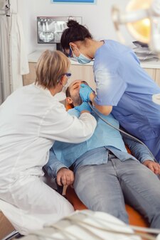 Starsza kobieta dentysta sprawdzająca z lustrem zdrowie chorego pacjenta