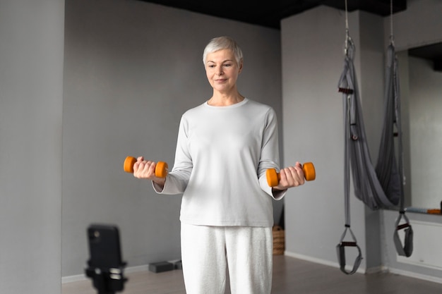 Starsza kobieta filmuje się podczas ćwiczeń fitness na siłowni