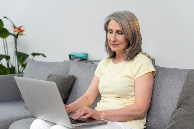 Starsza kobieta na kanapie w domu przy użyciu laptopa