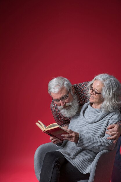 Starsza kobieta patrzeje jej męża patrzeje w książce przeciw czerwonemu tłu