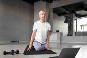 Bezpłatne zdjęcie starsza kobieta robi jogę na macie do jogi na siłowni
