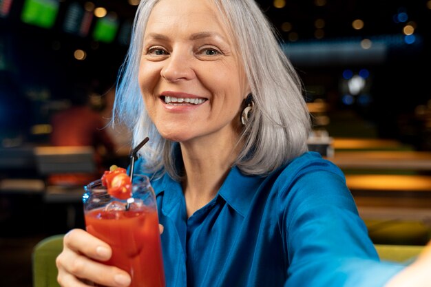 Starsza kobieta robi selfie z drinkiem w restauracji