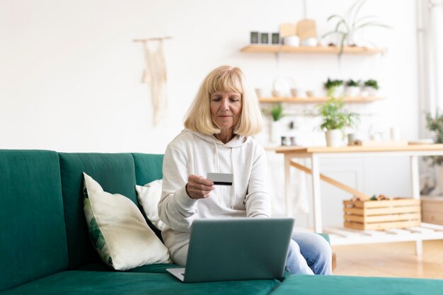Starsza kobieta robi zakupy online w domu z laptopem i kartą kredytową