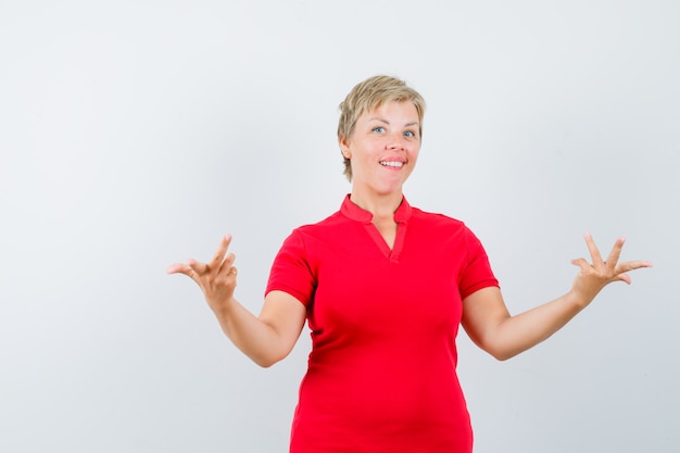 Bezpłatne zdjęcie starsza kobieta w czerwonej koszulce, rozciągając ręce w pytającym geście i patrząc niezdecydowany