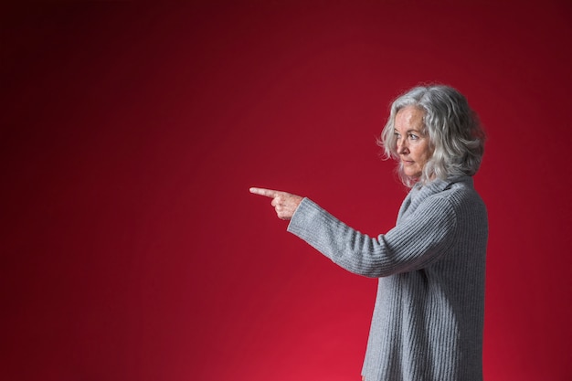 Starsza kobieta wskazuje jej palec przy coś przeciw czerwonemu tłu