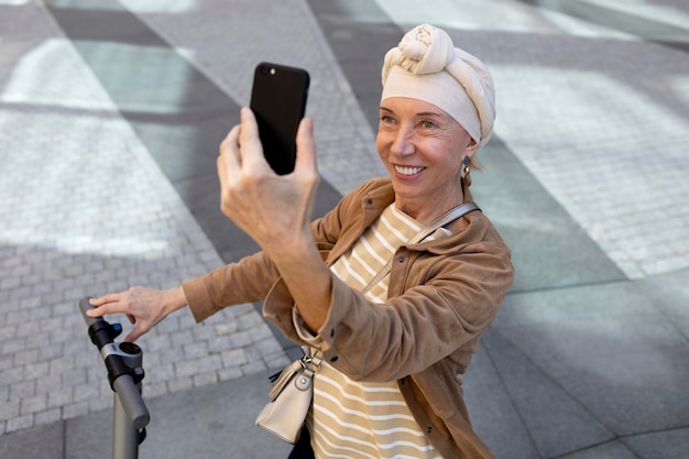 Bezpłatne zdjęcie starsza kobieta z elektryczną hulajnogą w mieście robi selfie