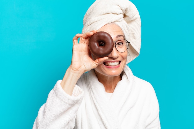 Starsza ładna kobieta po prysznicu, ubrana w szlafrok i jedząca śniadanie z pączkiem