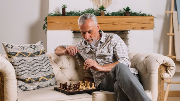 Starszego mężczyzna obsiadanie na kanapie bawić się szachy w domu