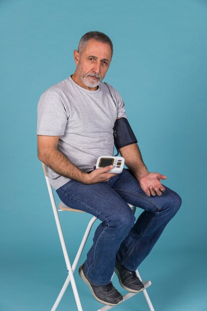 Starszego mężczyzna obsiadanie na krześle sprawdza ciśnienie krwi na elektrycznym tonometer
