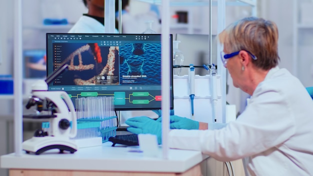 Starszy biochemik woaman sprawdzający objawy wirusa, pracujący w nowocześnie wyposażonym laboratorium. Zespół lekarzy badający ewolucję szczepionek przy użyciu zaawansowanej technologii badawczej diagnozy przeciwko Covid19